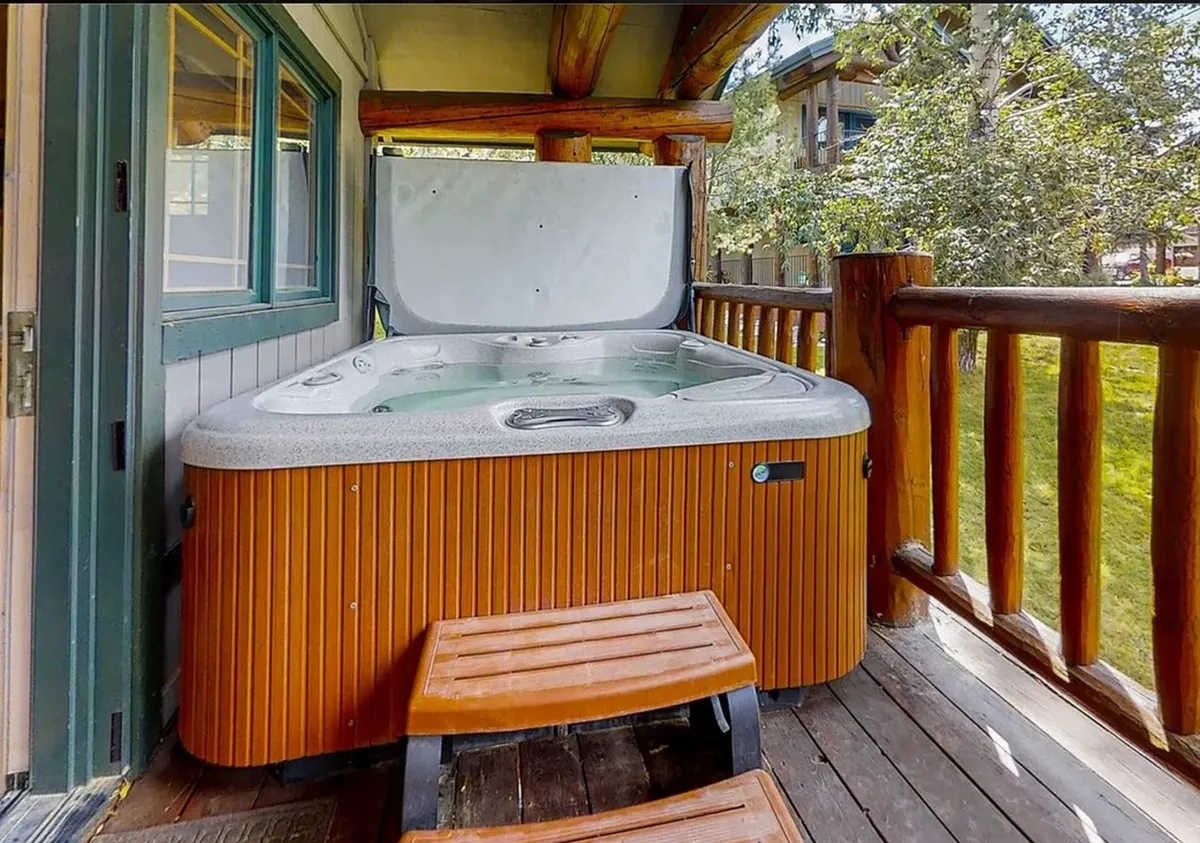 This image captures a private hot tub set on a spacious wooden deck, surrounded by lush greenery. The hot tub is positioned to invite stargazing or soaking in the fresh mountain air, while the deck’s ample space hints at al fresco relaxation and opportunities for socializing with friends. The overall mood is tranquil and inviting, perfectly echoing the wellness retreat vibe.