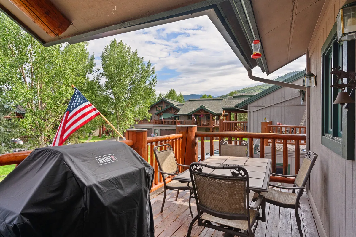 An exterior view featuring a spacious deck with a grill, dining table, and surrounding trees. The American flag adds a touch of character, and the setting is ideal for social gatherings after a day on the slopes.