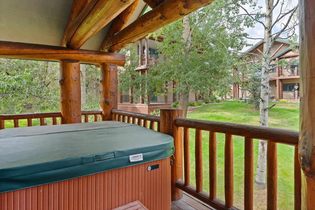 A hot tub sits tucked against a wooden structure, enveloped by green surroundings. The peaceful mood invites guests to unwind, whether under the stars or in the calm of the morning. This image emphasizes the harmonious connection between outdoor wellness and the natural environment.