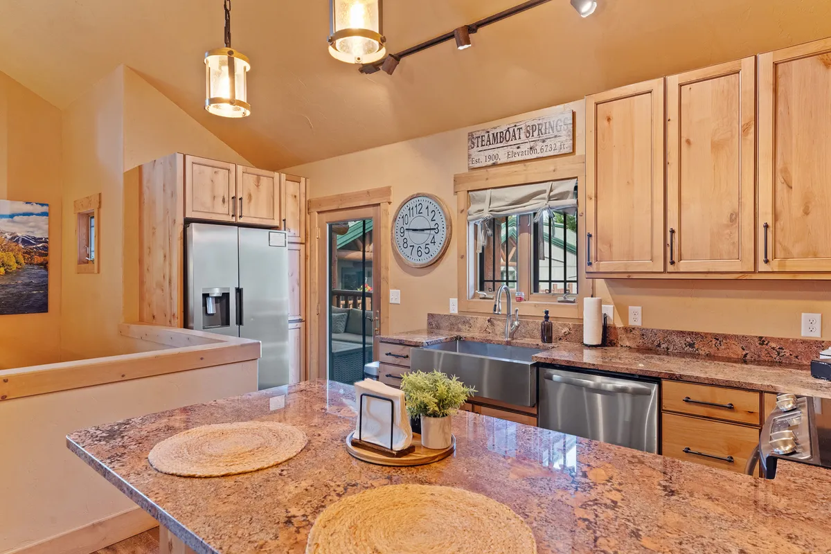 A modern kitchen with granite countertops, wooden cabinetry, and essential appliances. The space is ready for meal prep and entertaining, with a welcoming layout that invites guests to gather around and socialize while cooking or snacking.